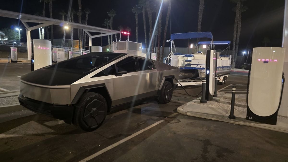 A silver Tesla Cybertruck is seen charging at a Tesla Supercharger station at night, showcasing its distinctive angular design and futuristic appearance.